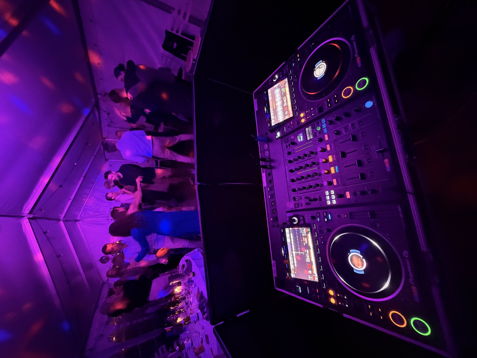 Gæster danser i et festtelt i lilla lys, set fra DJ-pulten