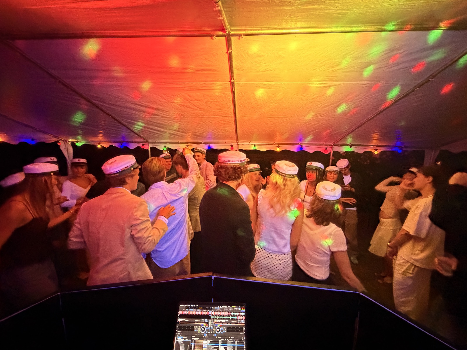 Studenter med huer danser i et farverigt oplyst festtelt